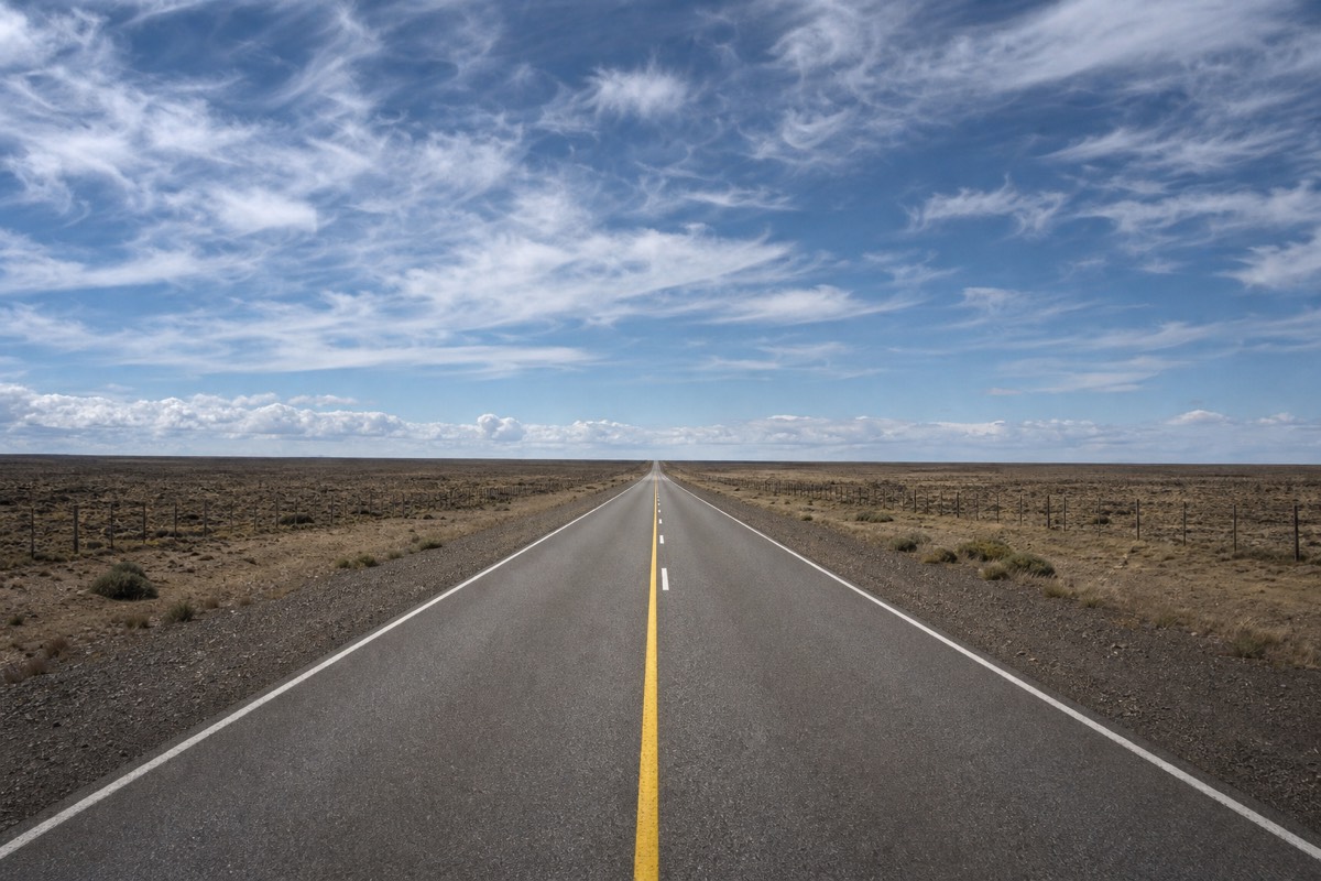 An empty road crossing open Patagonian steppe under a wide pale sky